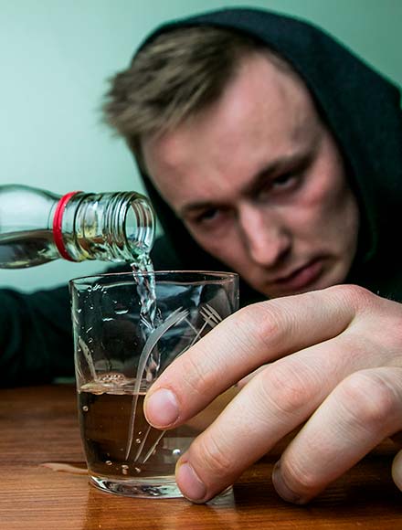 мужчина наливает водку в рюмку из бутылки